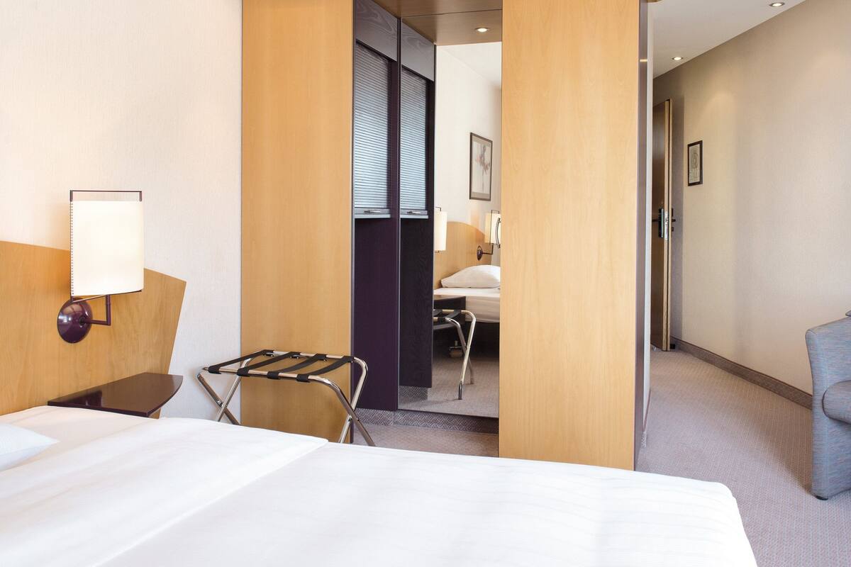 Une chambre d’hôtel avec un lit, un bureau, une chaise, une lampe et un vase de fleurs.