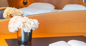 A hotel room with a bed, a bedside table with a vase of white flowers, and a mirror reflecting the bed and flowers. - Victor's Residenz-Hotel Frankenthal (Frankenthal)