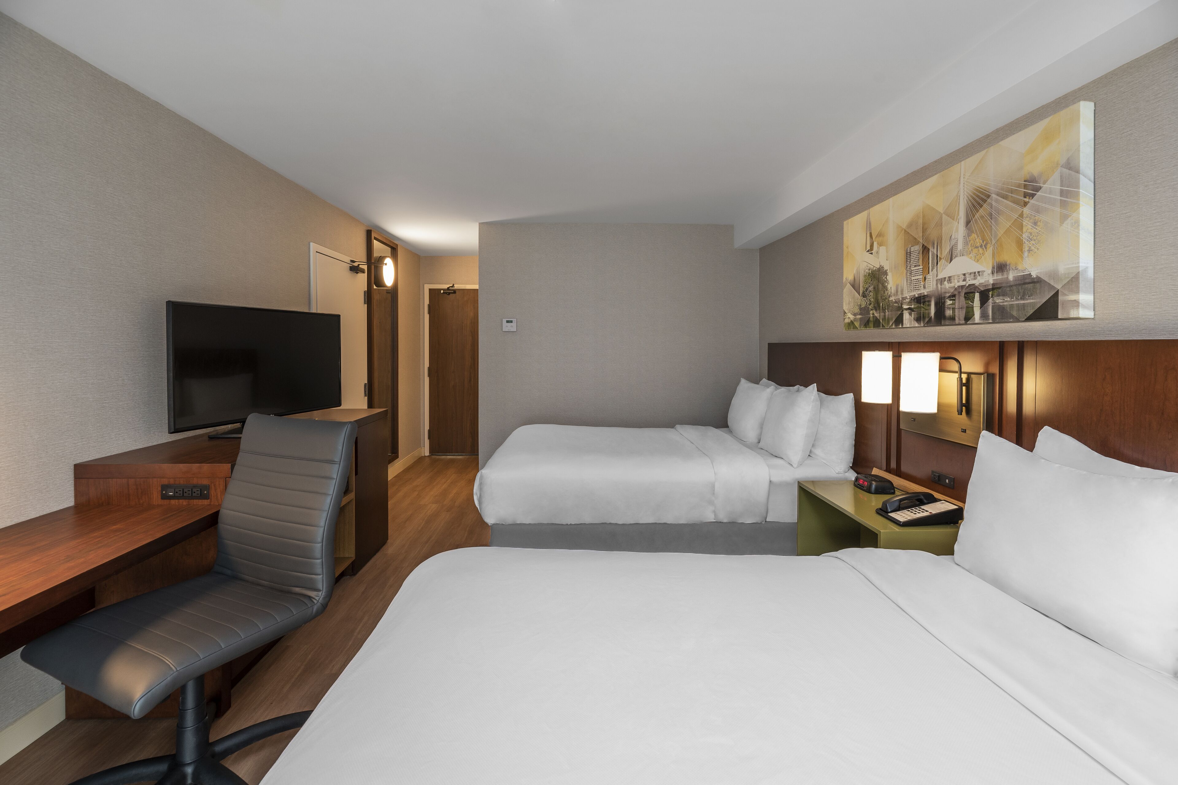A hotel room with two beds, a desk with a chair, a television, and a painting on the wall.