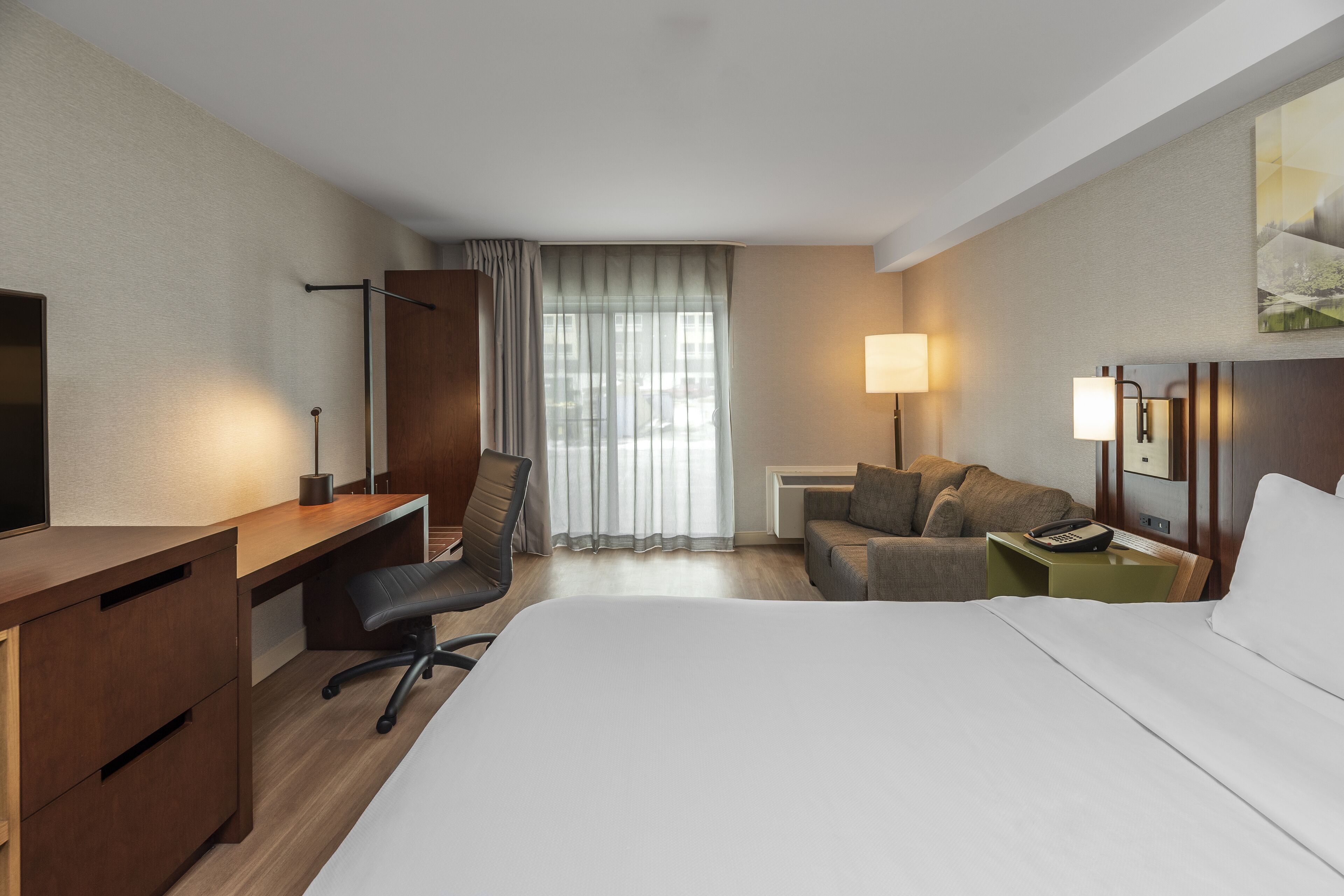 A hotel room with a bed, desk, chair, and a small sofa.