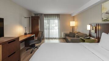 A hotel room with a bed, desk, chair, and a small sofa.