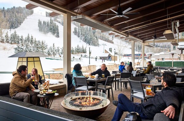 An outdoor seating area with a fire pit, tables, and chairs, overlooking a snowy mountain. - Park Hyatt Beaver Creek Resort and Spa (Avon)