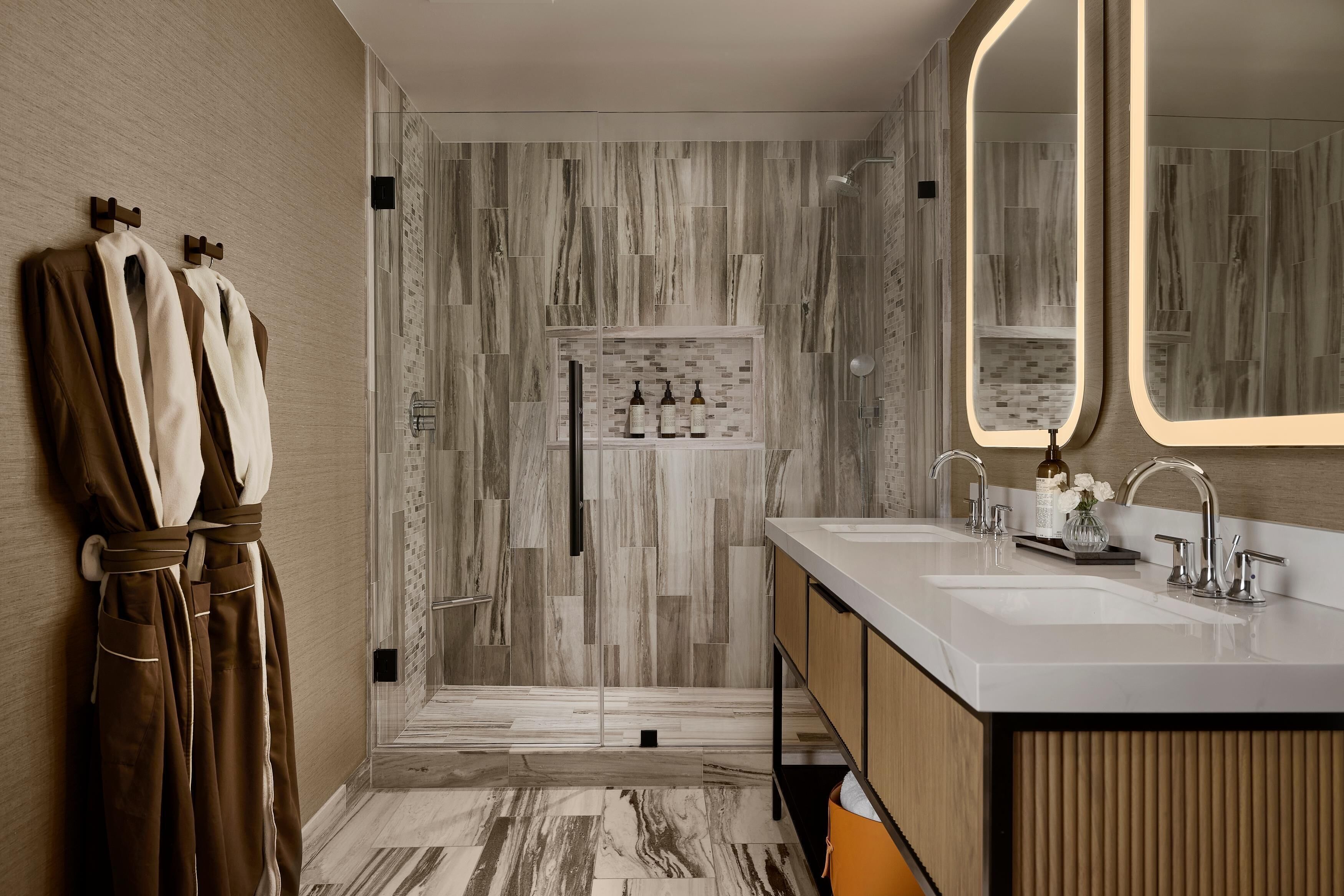 A modern bathroom with a double sink vanity, a large mirror, and a shower area with a tiled wall.