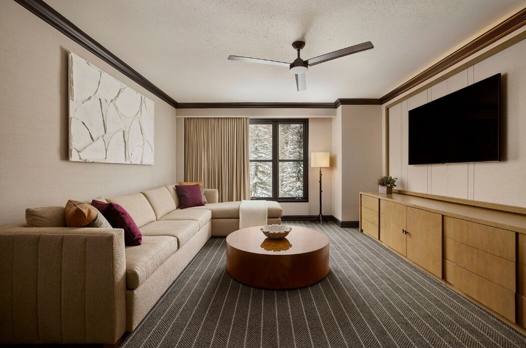 Un salon moderne avec un canapé, une table basse ronde, un téléviseur et un ventilateur de plafond.