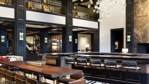 Un vestíbulo espacioso con un largo mostrador de recepción de madera, varios taburetes de bar y un techo alto con candelabros de cristal colgantes.