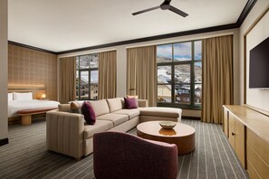 Une chambre d’hôtel comprenant un lit, un canapé, un fauteuil, une table basse ronde et un téléviseur.