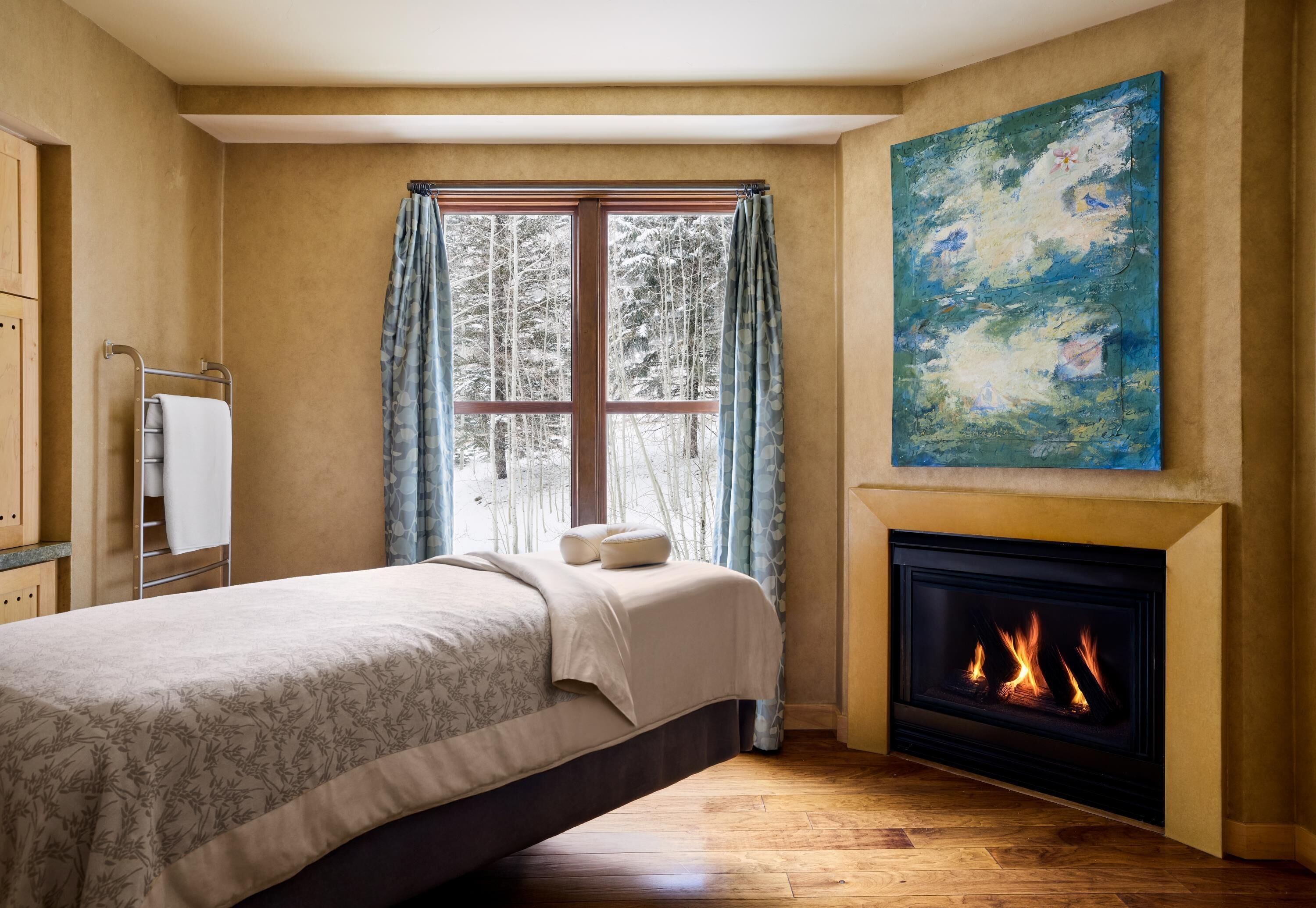 A bedroom with a bed, a fireplace, a window with curtains, and a painting on the wall.