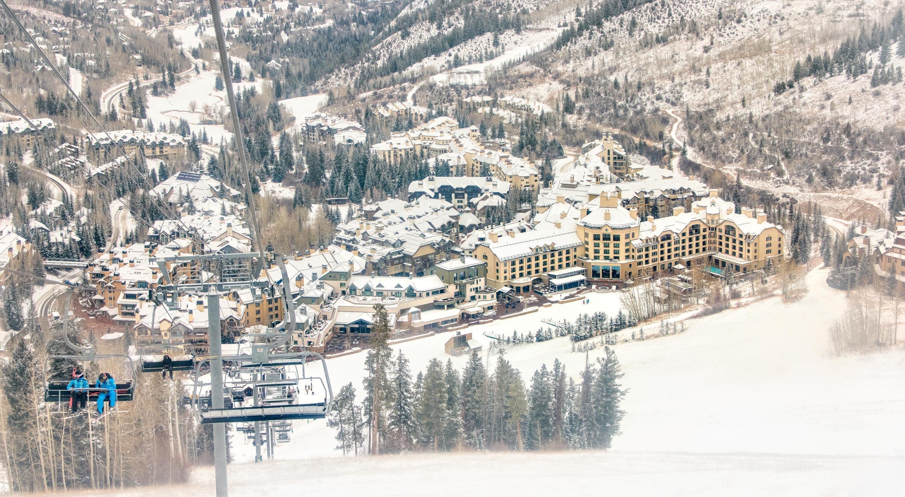 A snow-covered resort with multiple buildings, ski lifts, and a mountainous backdrop.