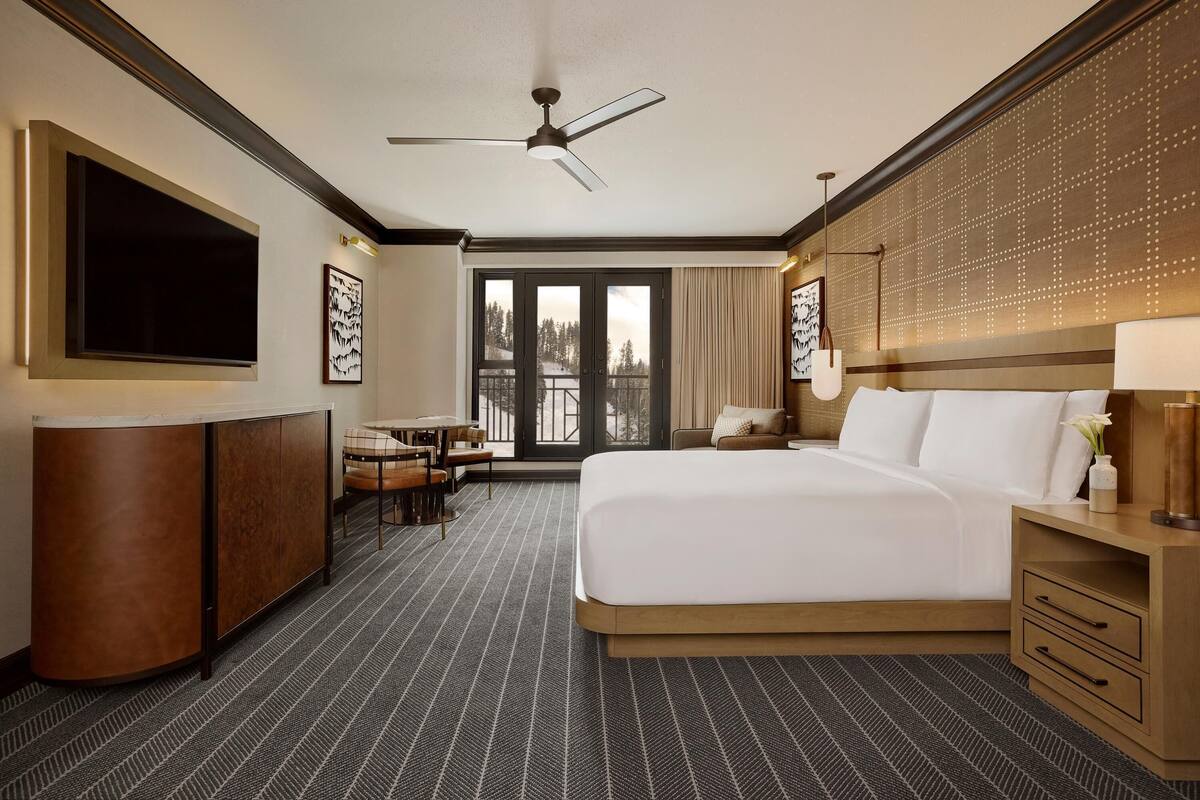 A hotel room with a bed, a desk, a chair, a TV, and a balcony with a view.