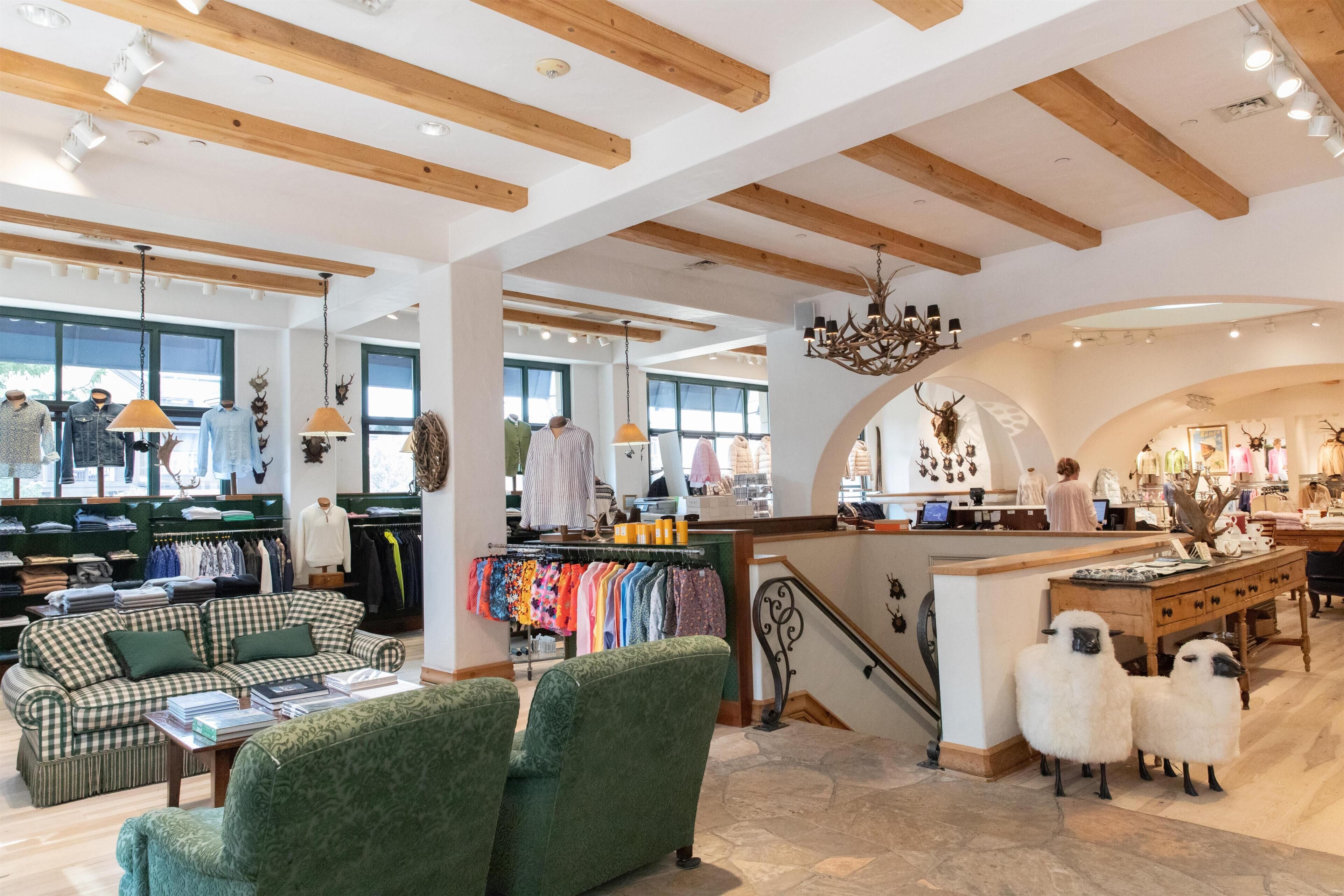 A spacious boutique hotel interior with high ceilings, exposed wooden beams, a central staircase, and a variety of clothing displays.