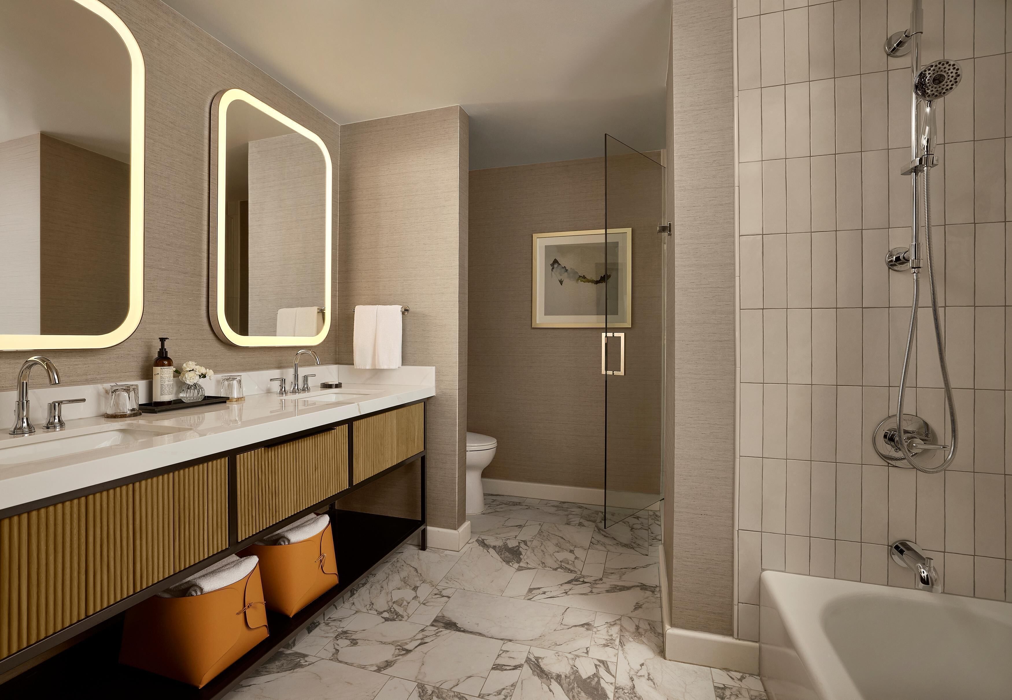 A modern bathroom with a large mirror, dual sinks, a shower, and a marble floor.