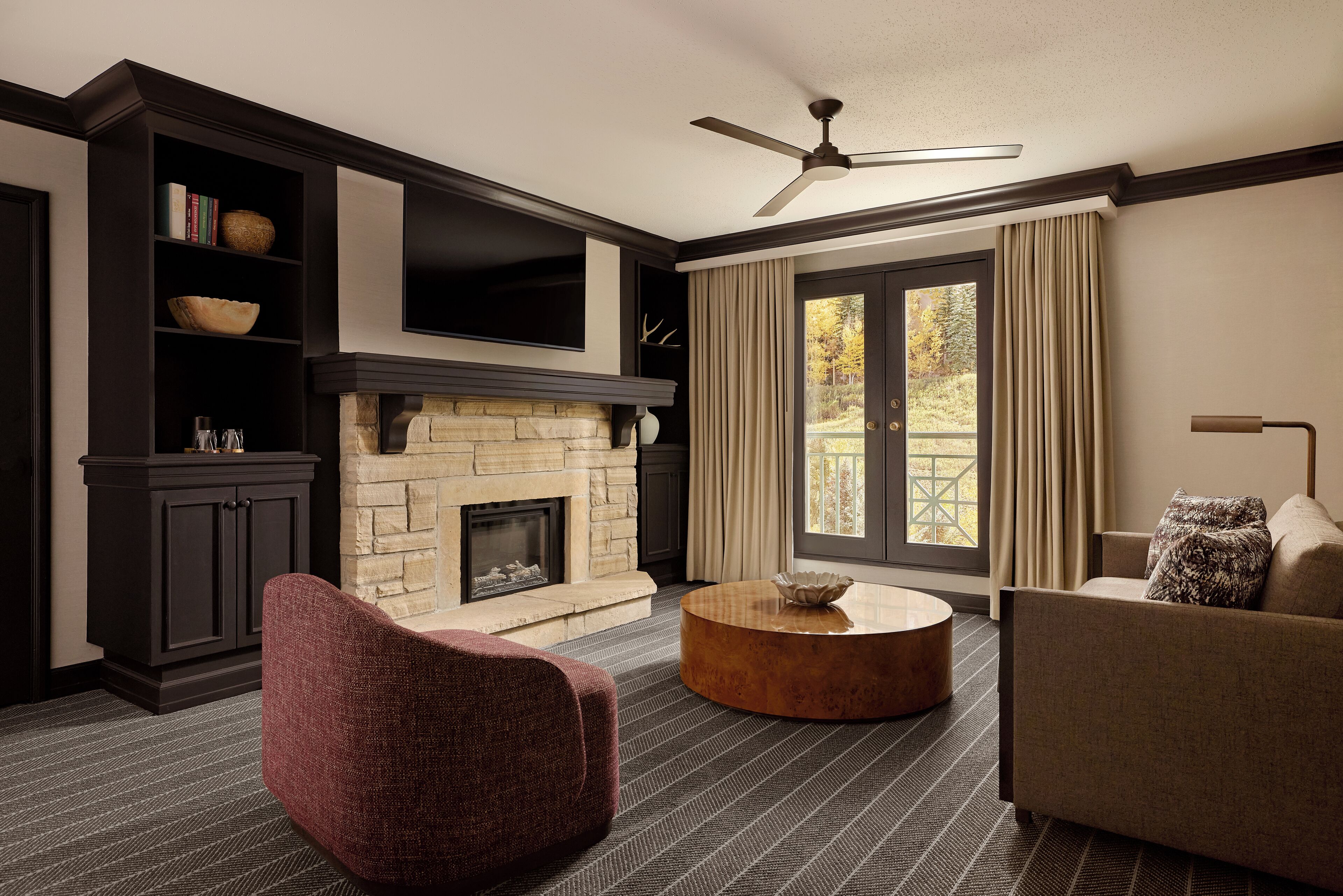 A living room with a fireplace, dark wood furniture, a round coffee table, and a large window with curtains.