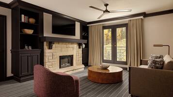 A living room with a fireplace, dark wood furniture, a round coffee table, and a large window with curtains.