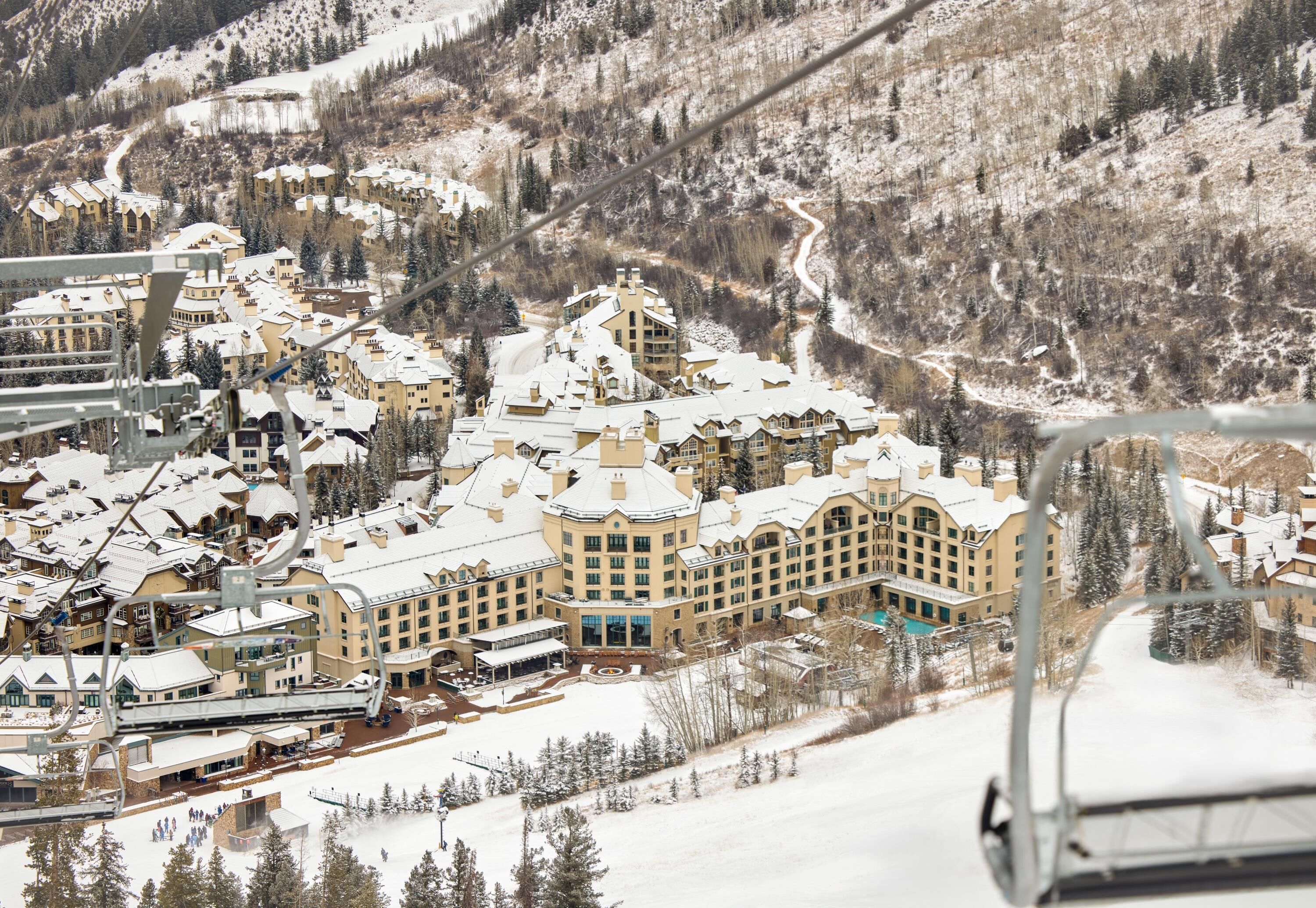 A snow-covered resort with multiple buildings, ski lifts, and a mountainous backdrop.