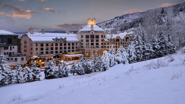 Un hotel grande de varios pisos con un edificio central y varias construcciones más pequeñas, rodeado de árboles nevados y un paisaje montañoso.