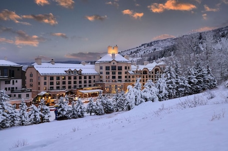 A large, multi-story hotel with a central building and several smaller structures, surrounded by snow-covered trees and a hilly landscape.