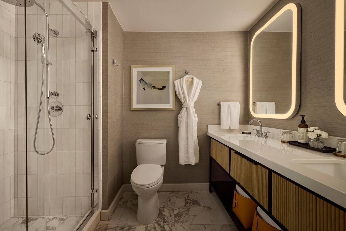 A modern bathroom with a glass-enclosed shower, a toilet, a sink with a mirror, and a framed artwork on the wall.