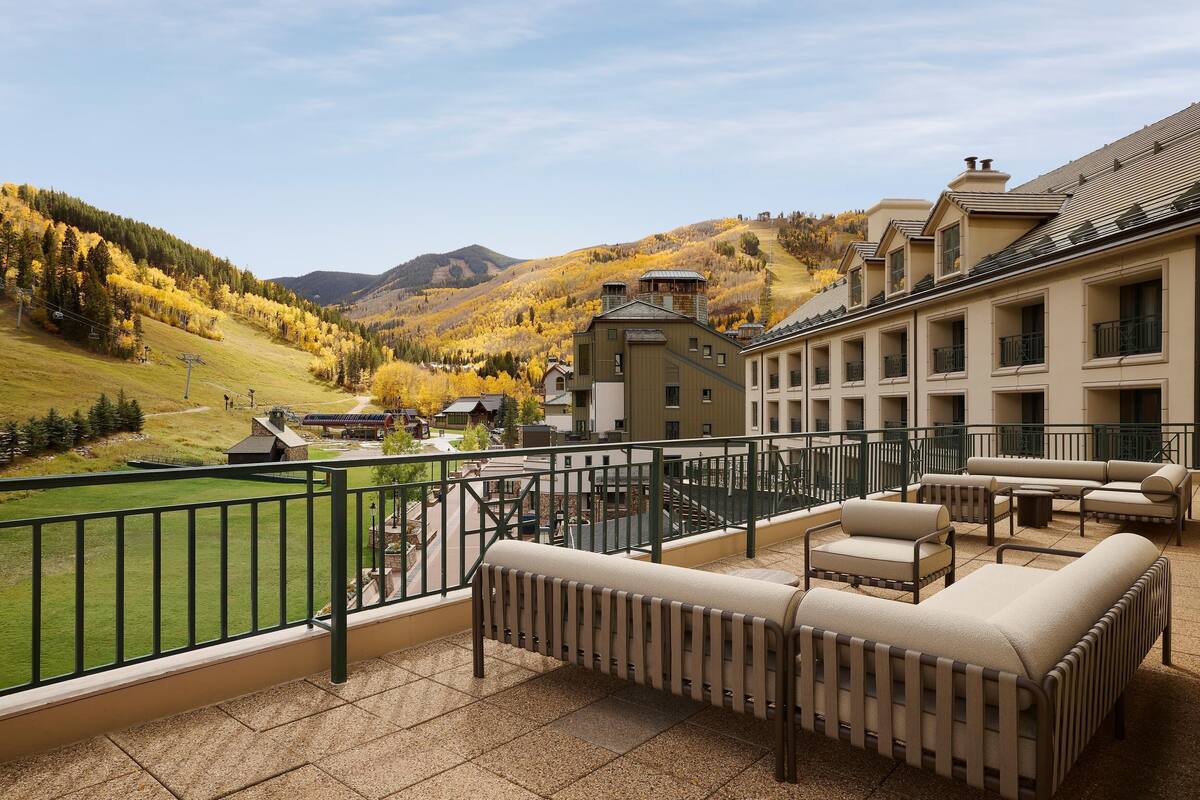 A balcony with outdoor seating, a view of a mountainous landscape, and a building with multiple windows.