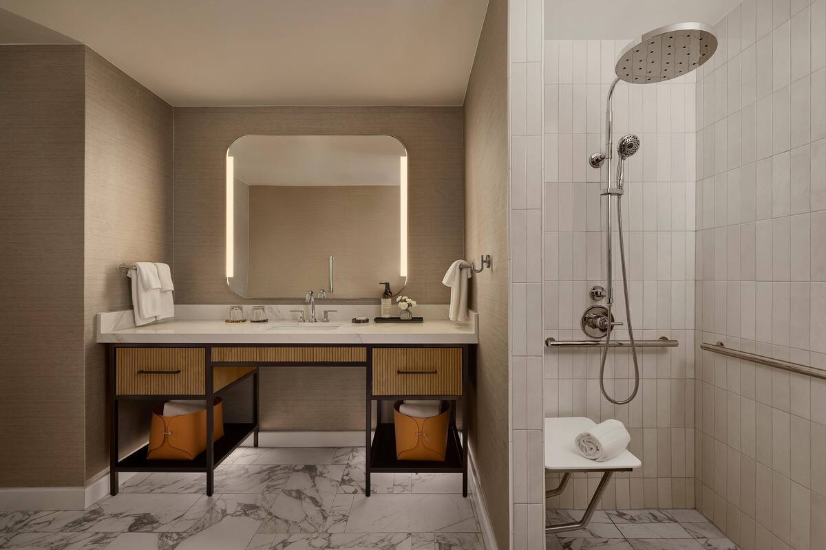 A modern bathroom with a marble floor, a large mirror, a shower, and a vanity with a towel rack.