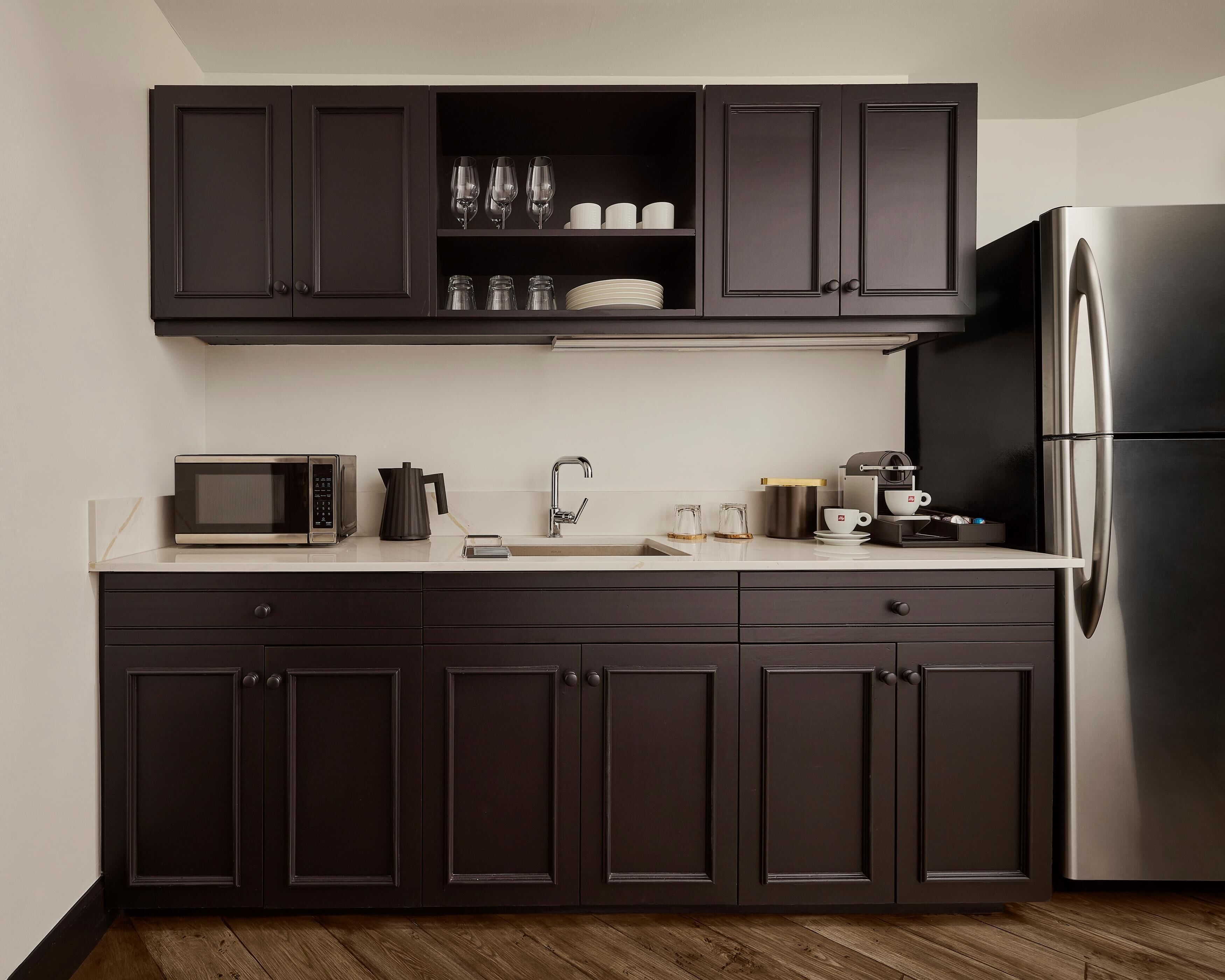 A modern kitchen with dark cabinets, a stainless steel refrigerator, a microwave, a coffee maker, and a sink.