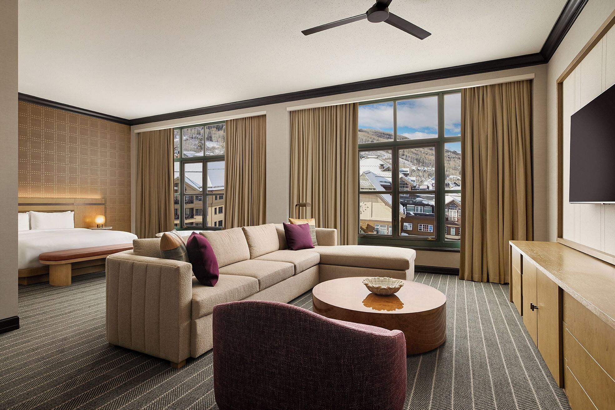 Habitación de hotel con cama, sofá, sillón, una mesa redonda de centro y televisión.