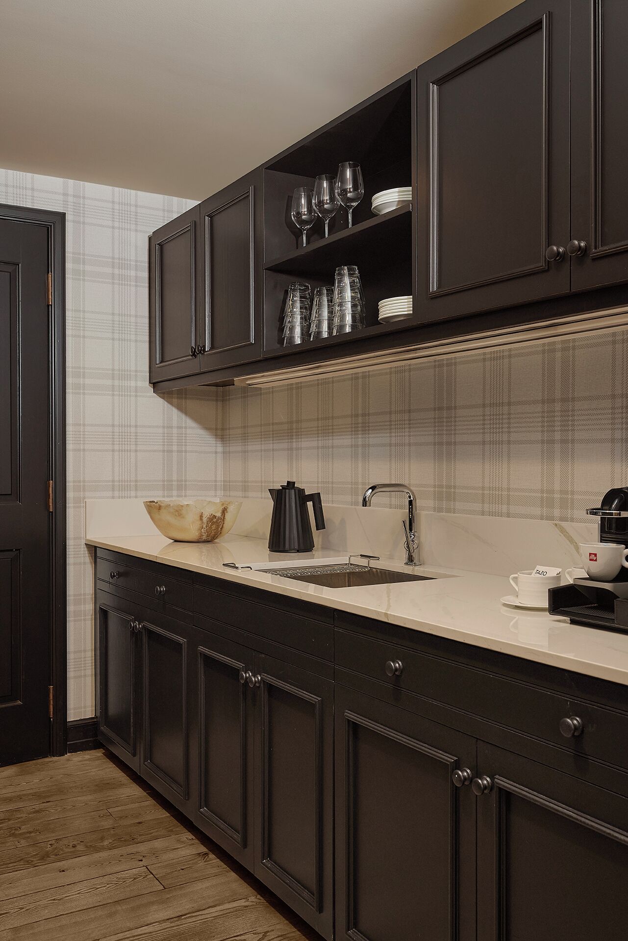 A kitchen with dark cabinetry, a white countertop, and a plaid-patterned backsplash.
