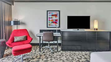A hotel room with a red armchair, a desk with a computer, a TV, and a cabinet.