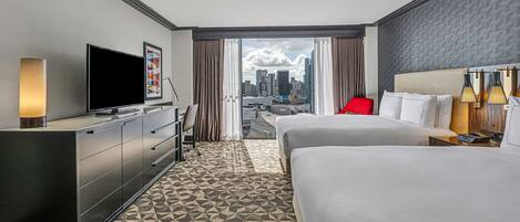 Habitación de hotel con una cama grande, televisión, escritorio y vistas a la silueta urbana.