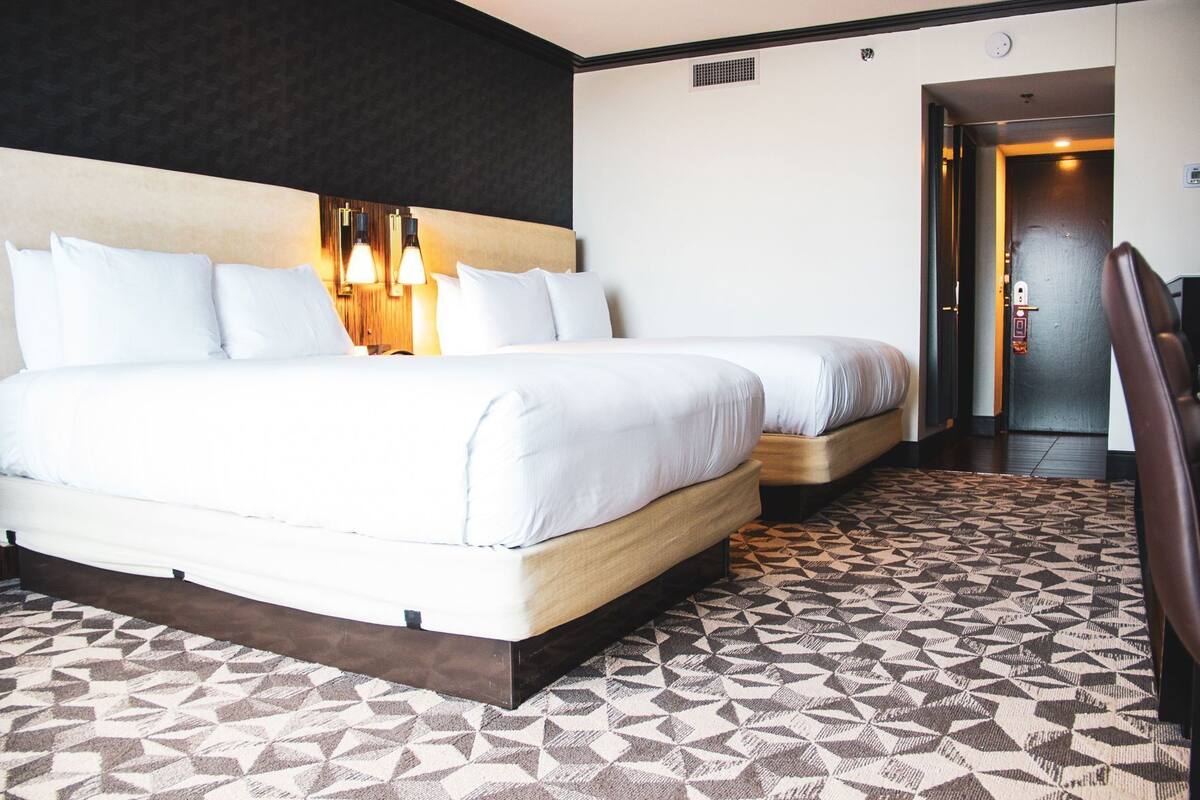 Une chambre d’hôtel avec un grand lit, deux lampes de chevet, une moquette à motifs et une porte donnant sur une autre pièce.