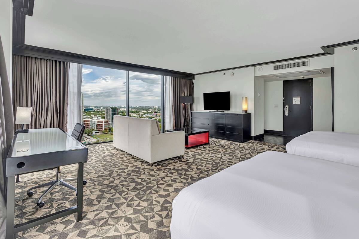 Une chambre d’hôtel avec une grande fenêtre, un bureau, une télévision, un lit et une armoire rouge.