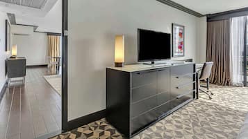 A hotel room with a modern design, featuring a large flat-screen TV, a desk with a chair, and a patterned carpet.