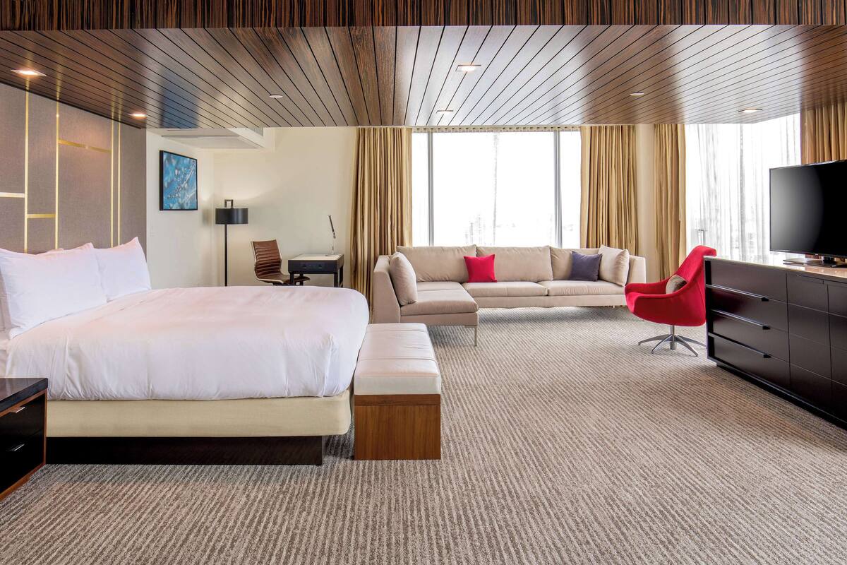 Une chambre d’hôtel avec un grand lit, un canapé, un fauteuil rouge, une télévision et un bureau.