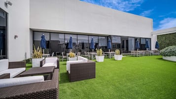 An outdoor patio with wicker furniture, potted plants, and umbrellas.