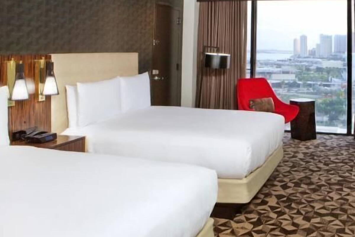 Une chambre d’hôtel avec deux lits, un fauteuil rouge, une télévision et une vue sur la ville.