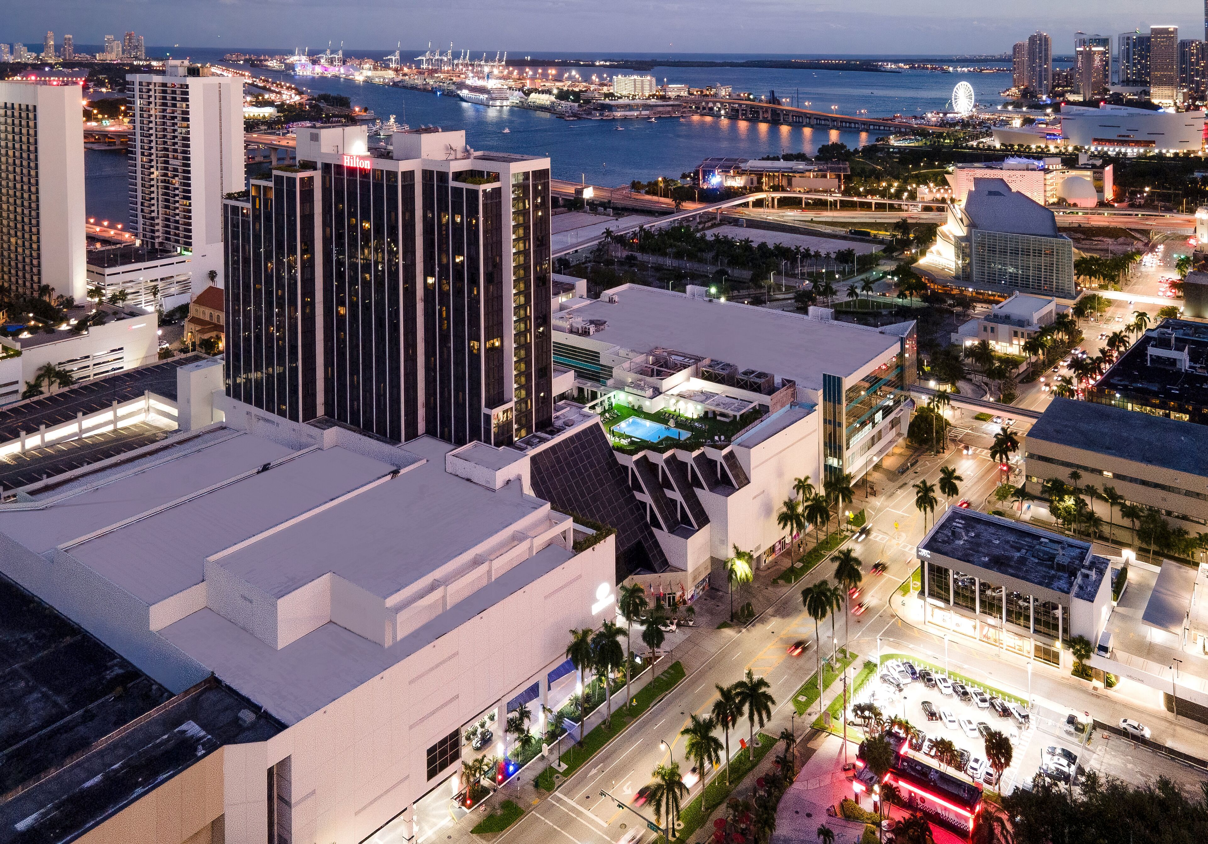 A high-rise hotel with a modern design, located near a waterfront with a view of the city skyline and a bridge.
