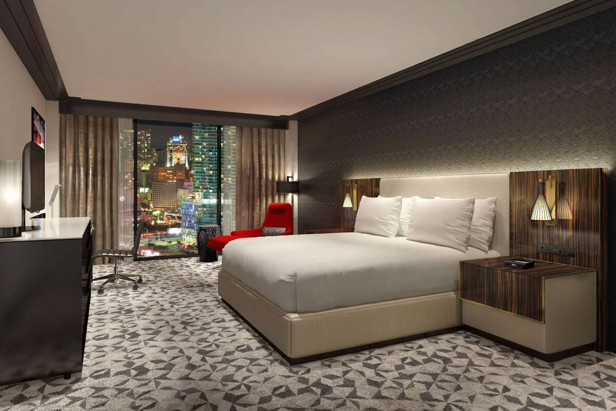 Une chambre d’hôtel avec un grand lit, un bureau, une chaise et une vue sur le paysage urbain illuminé la nuit.