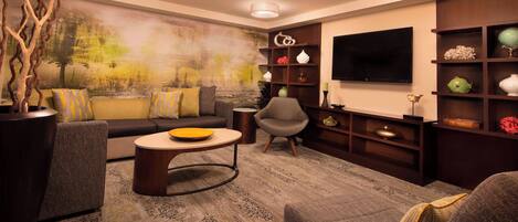 Una sala de estar moderna con sofá, sillones, una mesa de centro y televisor. Hay estanterías decorativas y un cuadro grande en la pared.