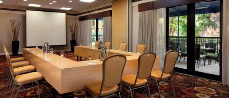 A conference room with a long table, chairs, a projector screen, and large windows with curtains.