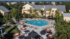 Un complejo turístico con piscina central, zona de estar al aire libre y palmeras.