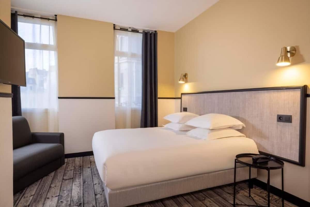 Una habitación de hotel con una cama, una pequeña mesa, un sofá y un televisor.