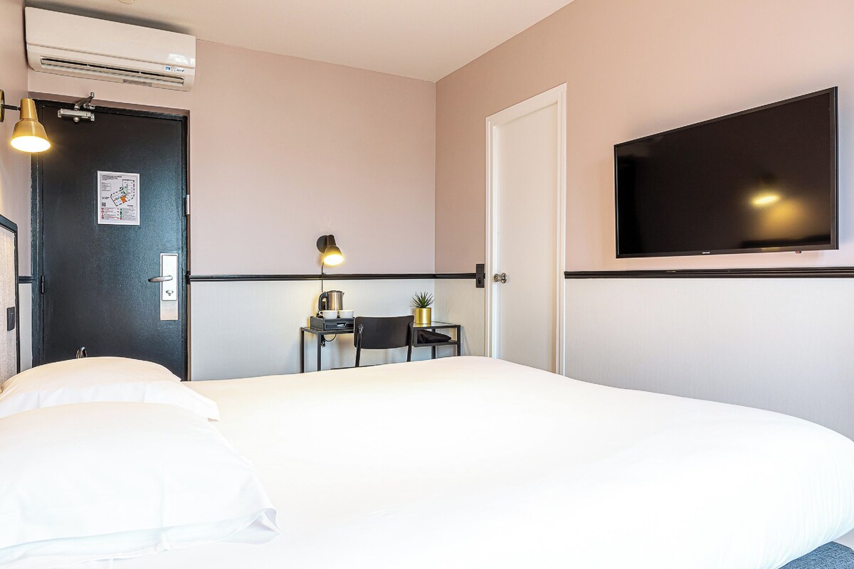 Een hotelkamer met een bed, een bureau, een stoel, een televisie en een airconditioning.