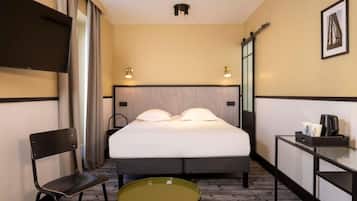 Una habitación de hotel con cama, una silla, una mesita, televisor y cafetera.