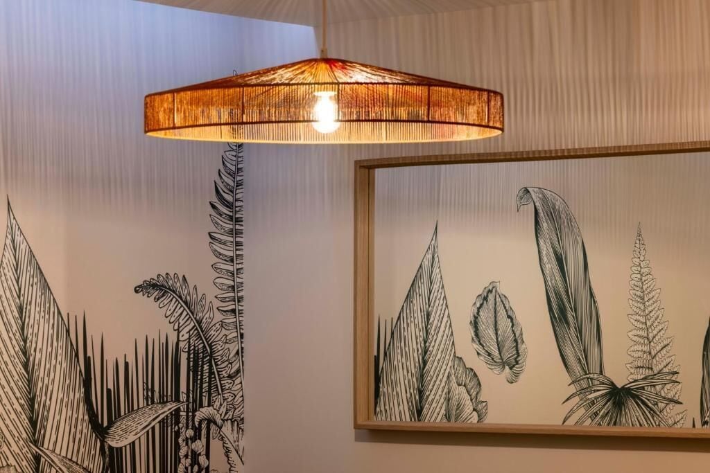 A room with a hanging light fixture and framed botanical illustrations on the wall.