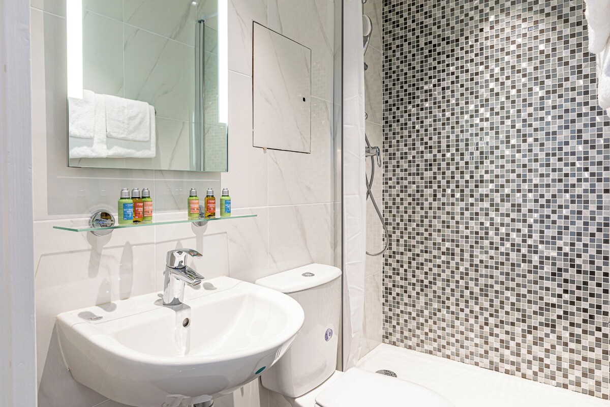 A bathroom with a white sink, mirror, and toilet. There are toiletries on a glass shelf.