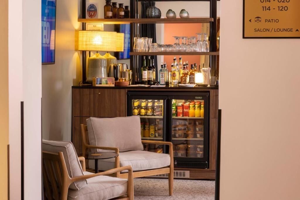 A bar area with a refrigerator stocked with beverages, a lamp, and shelves with glasses and bottles.
