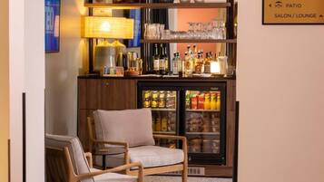 A bar area with a refrigerator stocked with beverages, a lamp, and shelves with glasses and bottles.