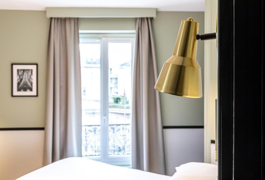 Ein Hotelzimmer mit Bett, einem Vorhangfenster und einem gerahmten Bild an der Wand.