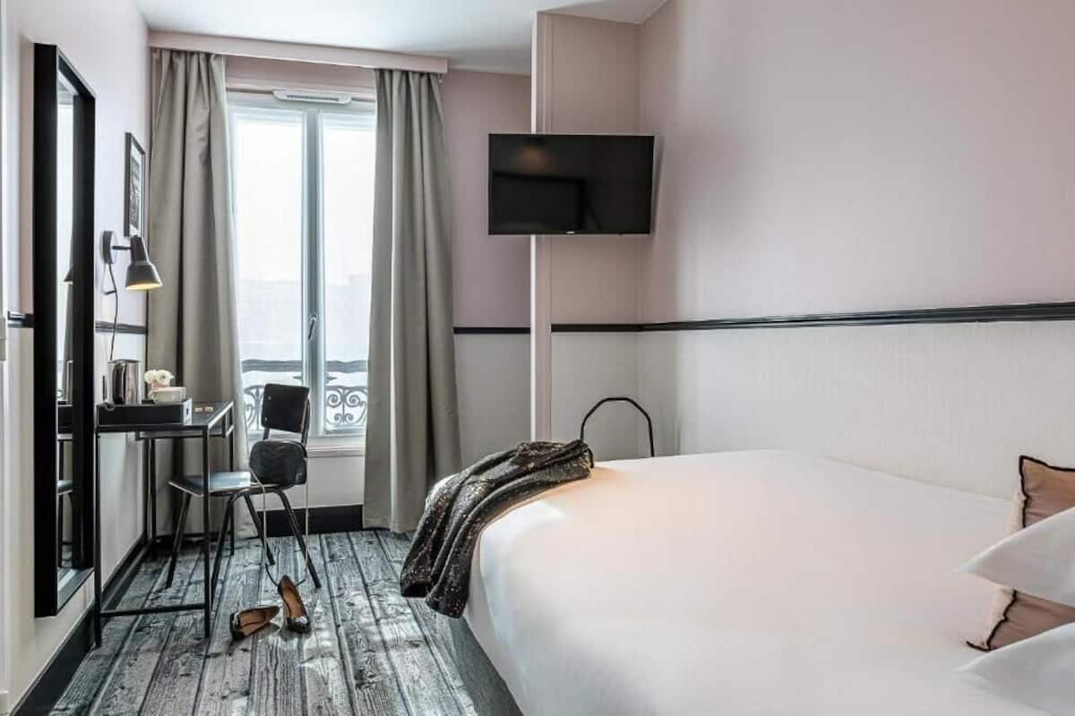 Habitación de hotel con cama, escritorio, silla, televisor y ventana con cortinas.