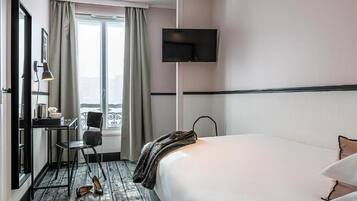 A hotel room with a bed, a desk, a chair, a TV, and a window with curtains.