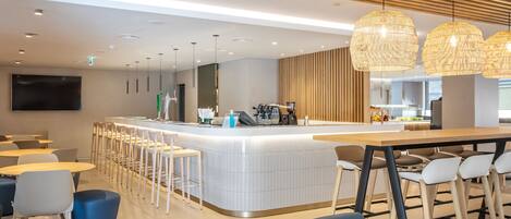 Zona de bar moderna con mostrador, taburetes e iluminación colgante.